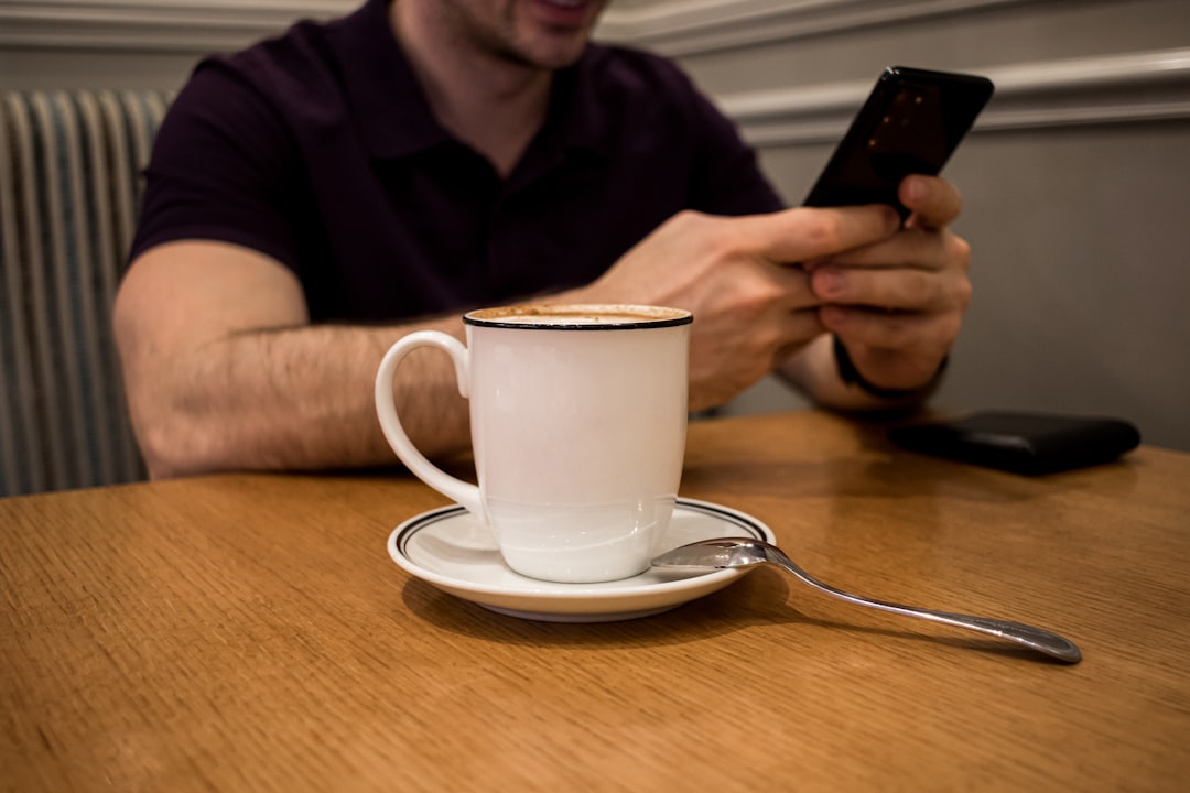 seseorang mengecek hasil togel di ponsel sambil minum kopi di kafe